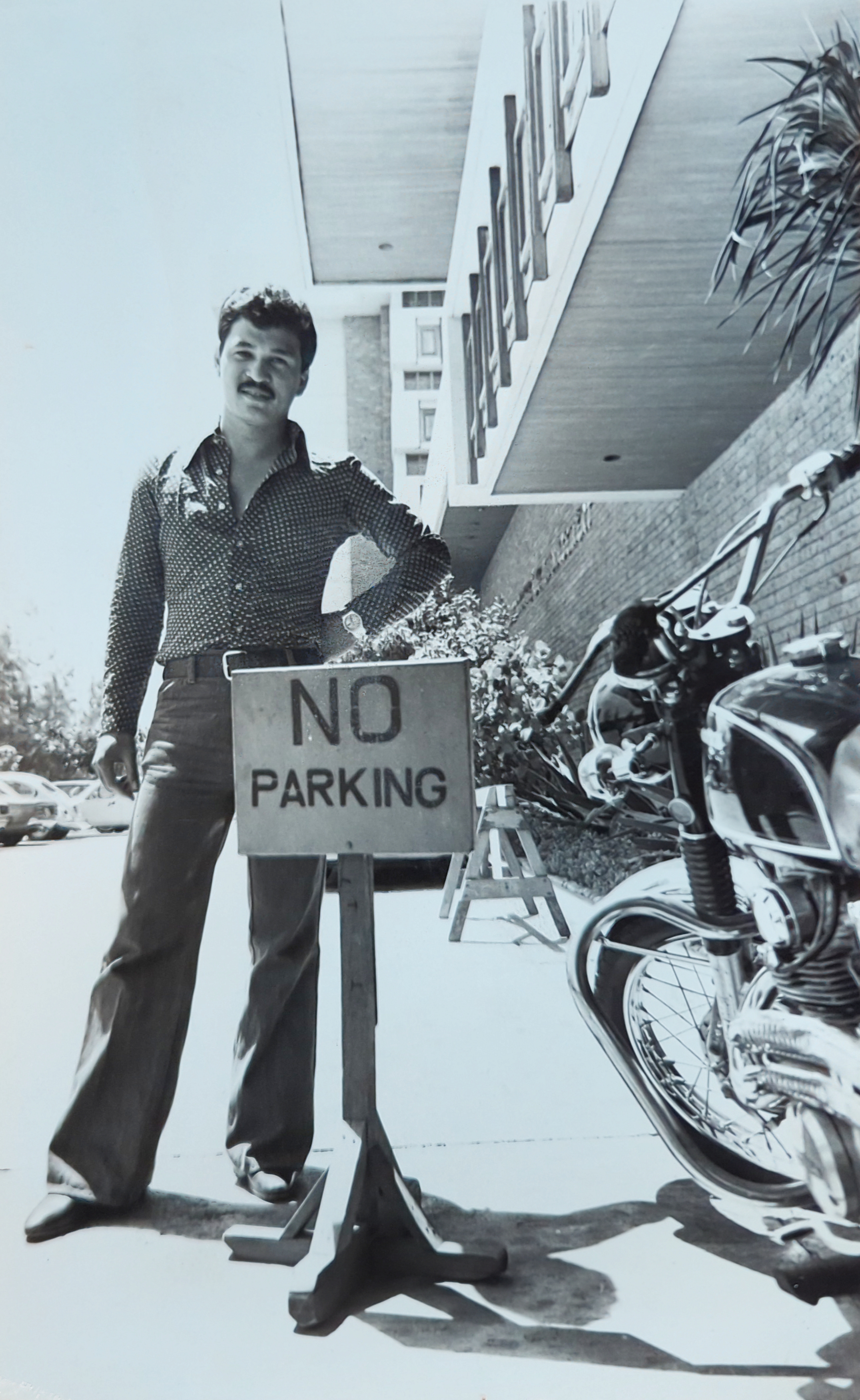 Black and white photo of Papa posing next to his motorcycle at a building at the Asian Institute of Management c. 1978